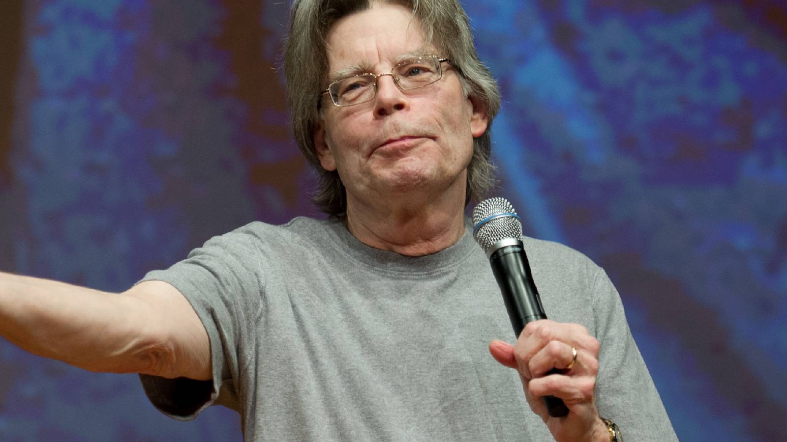 stephen-king-with-a-microphone-holding-out-his-arm.jpg