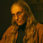 toni-collette-as-evelyn-smiling-suspiciously-while-sitting-at-a-table-in-wayward.jpg
